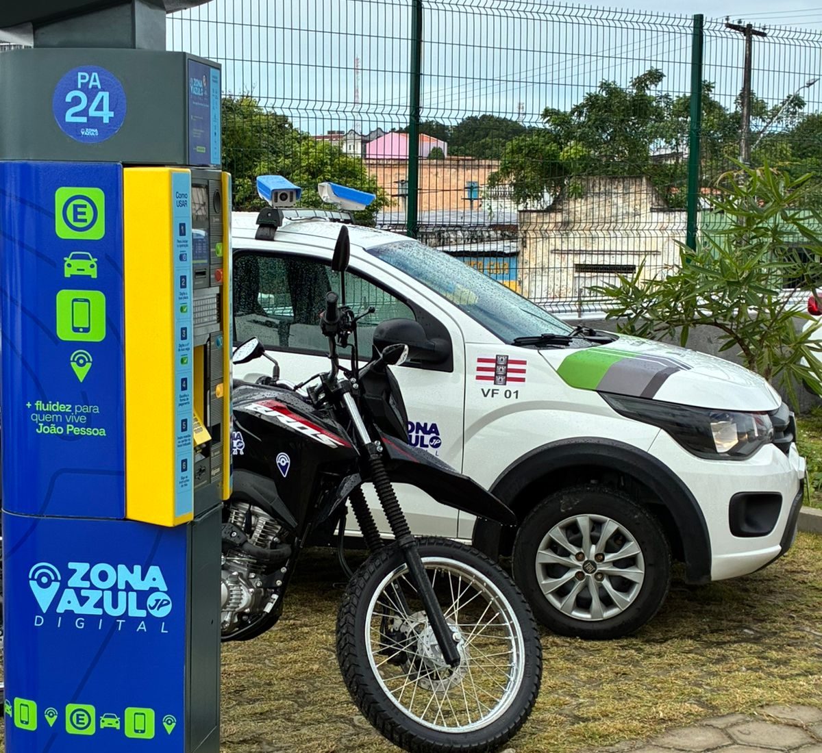 Carros estacionados em fila em uma avenida de João Pessoa com placas de sinalização da Zona Azul.