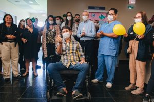 Paciente recebendo alta sob aplausos da equipe médica e de enfermagem no corredor do Hospital Metropolitano Dom José Maria Pires.