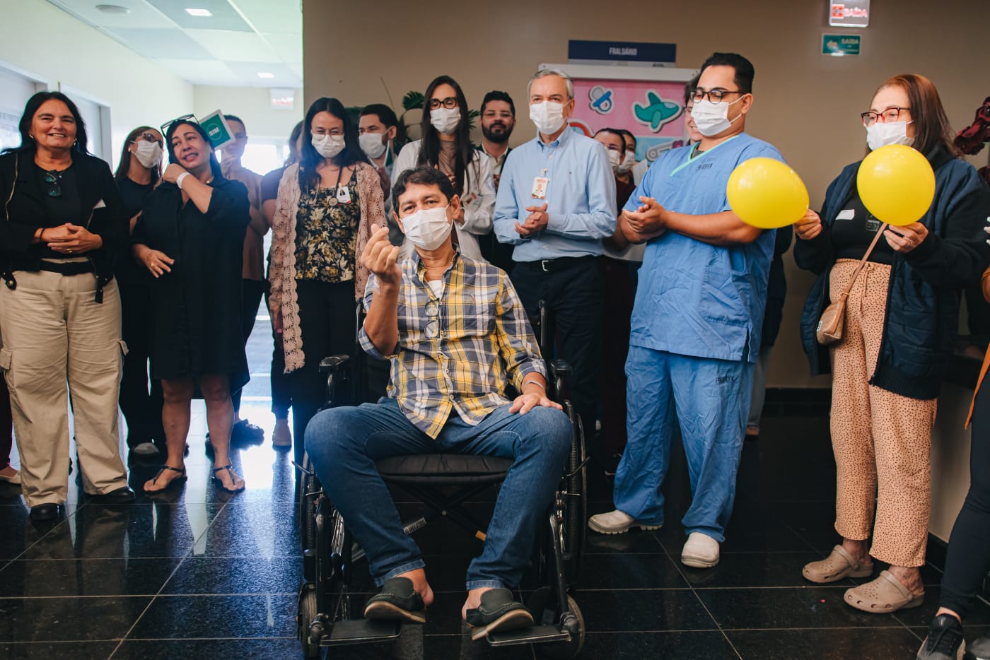 Paciente recebendo alta sob aplausos da equipe médica e de enfermagem no corredor do Hospital Metropolitano Dom José Maria Pires.