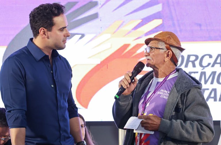 Governador Lucas Ribeiro discursando no palco da plenária do Orçamento Democrático Estadual no ginásio da escola Bráulio Maia.