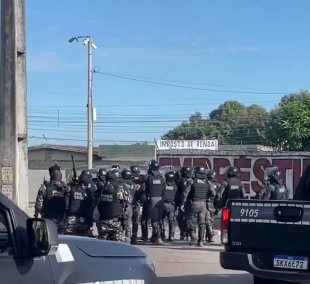 Viaturas da Tropa de Choque da Polícia Militar com luzes de emergência acionadas em rua bloqueada por protesto.