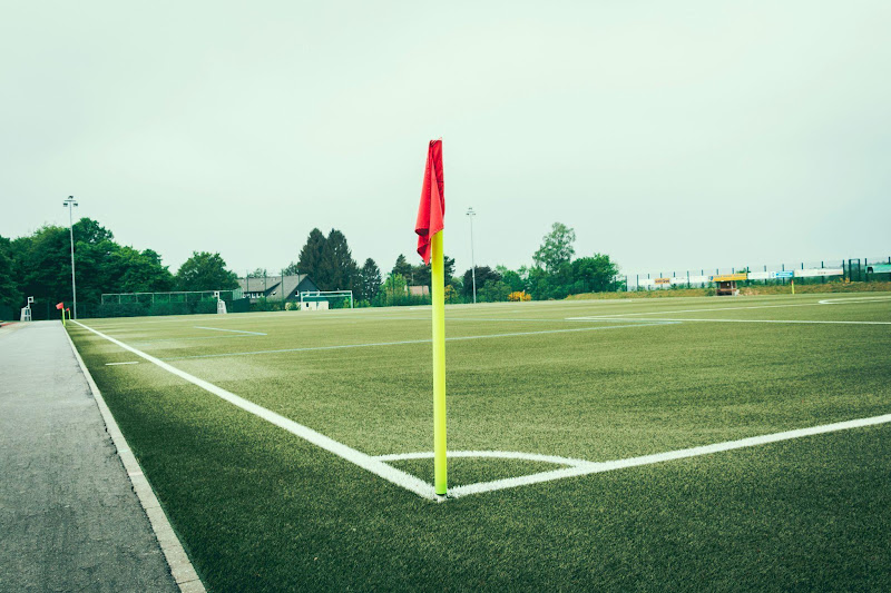Campo de futebol gramado, com linhas brancas demarcando o campo e uma bandeirinha ao centro da imagem.